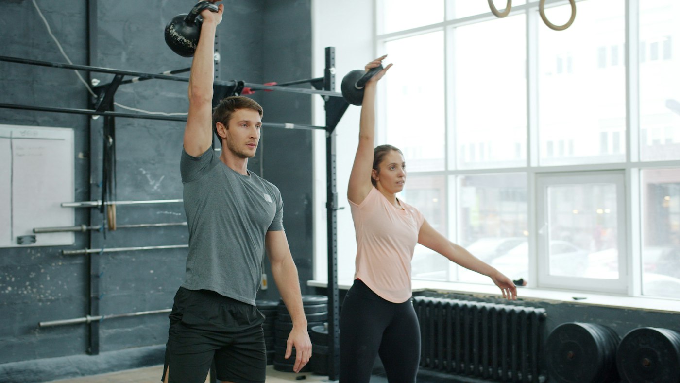 Two people training with barbells in a gym.